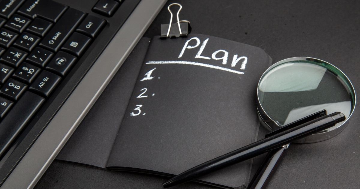 plan written black notepad clip pen magnifying glass black background