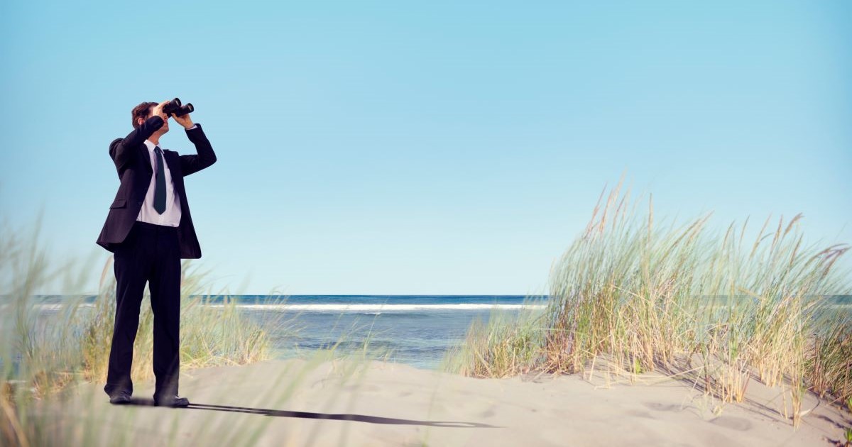 businessman with binoculars on beach looking out to sea