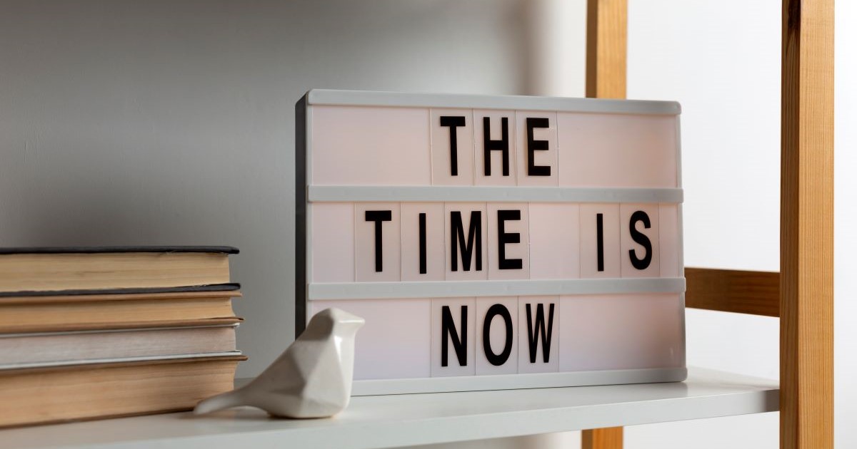 sign on bookshelf with words the time is now